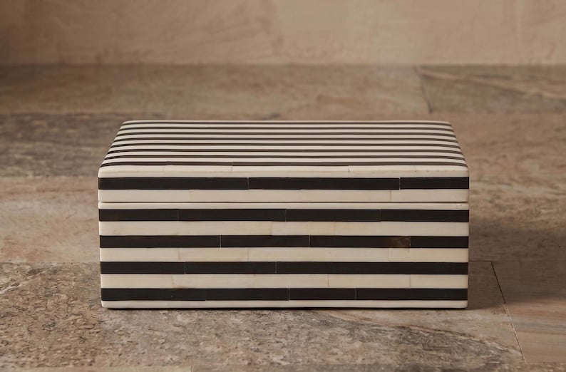May include: A rectangular storage box featuring a high-contrast pattern of horizontal black and white stripes. The box has a flat lid and a structured, boxy shape with visible seams between the individual rectangular pieces forming the striped exterior.