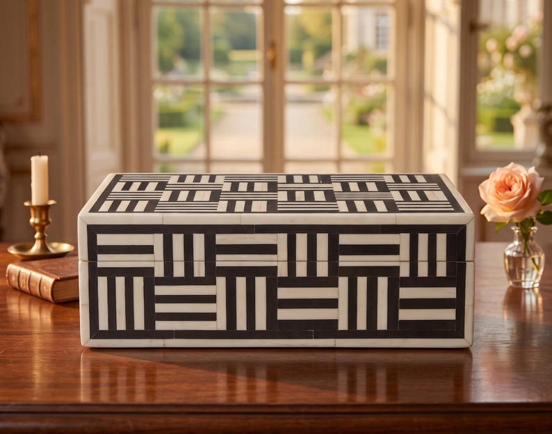 May include: A rectangular storage box featuring a high-contrast black and white geometric pattern. The exterior surface is composed of small, inlaid rectangular tiles arranged in alternating horizontal and vertical striped blocks across the lid and sides.