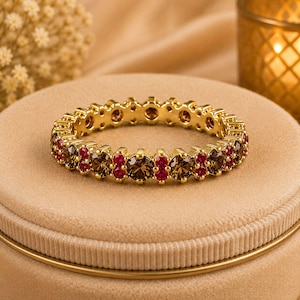 May include: A gold eternity band featuring an alternating pattern of round-cut brown smoky quartz gemstones and smaller round-cut vibrant red rubies set in a continuous circular design with a polished metallic finish throughout the entire ring.