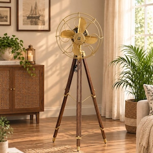 May include: A floor-standing fan featuring a circular gold-toned metal cage and four matching gold-toned blades. The fan is mounted on a dark brown wooden tripod base with gold-toned metal hardware accents and a central circular logo plate.