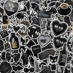 Peut inclure: Une collection d'autocollants en noir et blanc avec des images gothiques, dont des crânes, un cœur avec le texte 'TIL WE ARE GHOSTS', un dé noir avec des crânes, une bouteille étiquetée 'CEMETERY DIRT', un cercueil, une peluche chat et du whisky.
