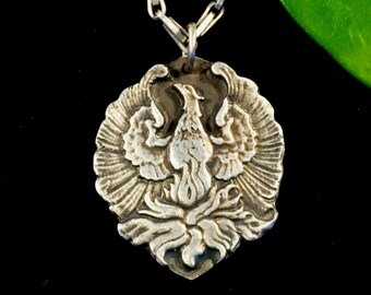 May include: A silver pendant necklace featuring a detailed, three-dimensional design of a phoenix rising from flames. The pendant is attached to a silver chain.