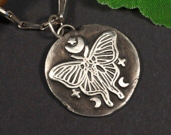 May include: A silver necklace with a round pendant featuring a detailed etched design of a butterfly with crescent moons and stars.