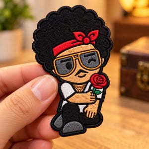 May include: An embroidered patch featuring a cartoon character with a large black afro hairstyle, wearing a red headband, gold-rimmed sunglasses, and a white shirt. The character has a mustache and is holding a single red rose.