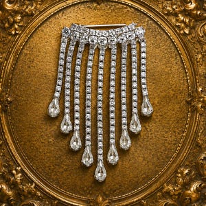 May include: A silver-toned brooch featuring a curved top bar encrusted with clear round rhinestones. Eight dangling strands of rhinestones descend from the bar, each ending in a single pear-shaped crystal drop, creating a cascading fringe effect.