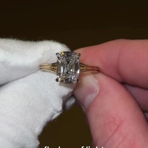 Puede incluir: Un anillo de oro con una gran piedra central de corte cojín rectangular con bordes facetados. La banda está formada por varios hilos de oro finos y paralelos que convergen en el engaste, creando un aspecto delicado y estructurado.