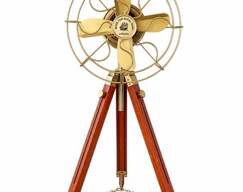 May include: A brass desk fan with four blades and a circular wire cage, mounted on a three-legged wooden tripod stand. The center of the fan features a circular emblem with the text MADE FOR ROYAL NAVY LONDON and a ship illustration.