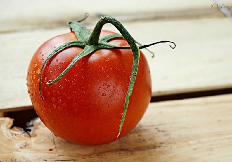 May include: A single, ripe red tomato with a green stem and water droplets on the surface. The tomato is sitting on a wooden surface.