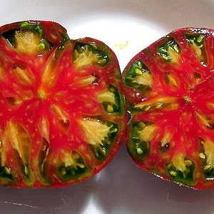 May include: A close-up of a halved tomato with a red and green striped pattern. The tomato has a starburst shape with a yellow center.