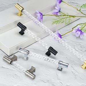 Puede incluir: Cuatro tiradores de armario con barras de acrílico transparente trenzado y bases metálicas en acabados dorado, negro mate, cromo pulido y níquel cepillado. Cada tirador presenta un diseño cilíndrico con placas de montaje cuadradas.