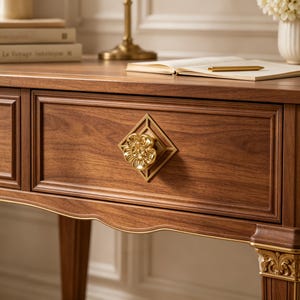 May include: A wooden console table featuring a rich brown grain, a rectangular drawer with a gold-toned flower-shaped knob centered on a diamond-shaped backplate, and ornate gold-toned carved detailing on the top of the fluted table legs.