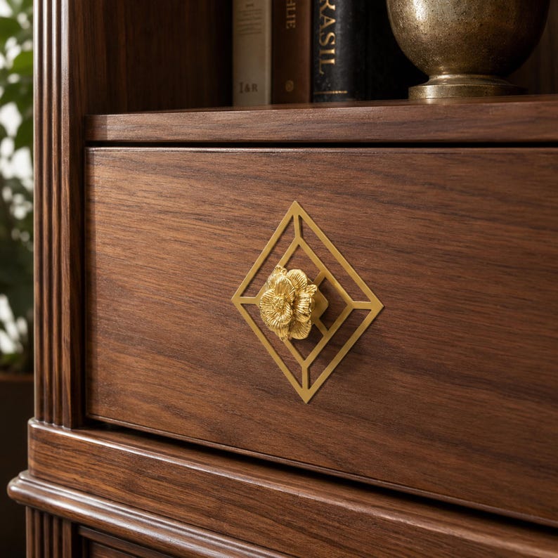 May include: A dark brown wooden drawer featuring a gold-colored metal geometric diamond-shaped inlay centered around a three-dimensional gold floral knob. The drawer is part of a larger wooden cabinet structure with vertical fluted side detailing.