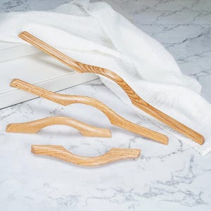 May include: Four light-colored wooden cabinet handles with a natural grain pattern. The handles feature a curved, organic shape with varying lengths, ranging from a long, slender design to shorter, more compact arched pieces.