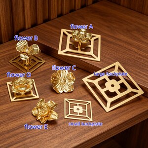 May include: A collection of gold-toned metal cabinet knobs and backplates. The set includes flower A, flower B, flower C, flower D, and flower E designs, along with a large backplate and a small backplate, each featuring geometric cutouts.