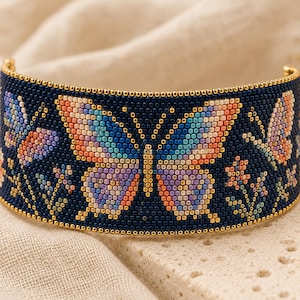 May include: A wide cuff bracelet crafted from dark navy blue seed beads. The design features a central butterfly with wings in gradients of orange, blue, and purple, flanked by smaller butterflies and floral motifs in matching vibrant colors.