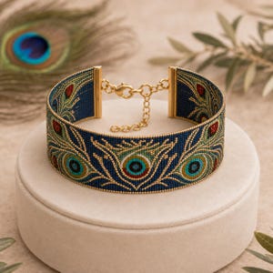 Puede incluir: Una pulsera ancha de tipo brazalete hecha con pequeñas cuentas sobre una base azul oscuro, con un patrón repetitivo de plumas de pavo real en tonos verde azulado, verde, dorado y rojo. Incluye un cierre de mosquetón y cadena dorados.