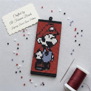 May include: A rectangular beaded keychain featuring a pixelated character design in red, black, white, and blue. The piece includes a small loop at the top. A white card with the text Crafted by Al-Faisam Beads Keyring Bead Loom Pattern is visible.