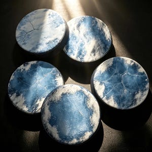 May include: Five circular coasters featuring a blue and white color palette. Each coaster displays a unique pattern, including cracked ice textures, swirling clouds, and delicate snowflake motifs, creating a cohesive winter-themed set.