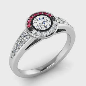 May include: A silver-toned ring featuring a large central round-cut white stone surrounded by a halo of smaller red and white stones. The band is accented with additional small white stones along the shoulders, set in a polished metal finish.