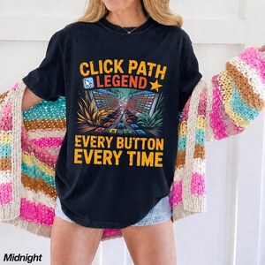 May include: A black short-sleeve t-shirt featuring the yellow and orange text CLICK PATH LEGEND EVERY BUTTON EVERY TIME. The graphic includes a computer cursor icon, a star, and a stylized illustration of a complex digital interface with red lines.