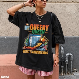 May include: A black oversized t-shirt featuring a graphic print with the text QUEERY QUEEN and SELECT STAR FROM CHAOS. The design includes a stylized spreadsheet grid, a golden crown, and colorful abstract elements in orange, blue, and green.