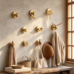 Puede incluir: Una colección de ganchos de pared dorados con diversas formas, incluyendo una cabeza de zorro, un pez dorado, una libélula, una concha, una mariposa, una cabeza de ciervo, una hoja de arce y un caracol montados en la pared.