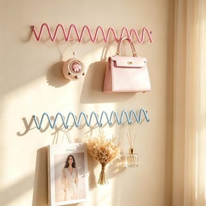 Puede incluir: Dos estantes de pared de metal con diseño en zigzag, uno rosa y otro azul claro. El estante rosa sostiene un colgante redondo y un bolso rosa claro. El estante azul claro sostiene una fotografía enmarcada, un ramo de flores secas y un difusor.