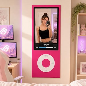 Puede incluir: Un espejo de pared de cuerpo entero diseñado para parecerse a un reproductor de música digital rosa. El espejo cuenta con una gran superficie reflectante rectangular con una interfaz de control circular blanca debajo.