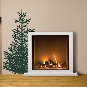 May include: A modern white fireplace with a burning fire, set against a neutral wall. A dark green fir tree silhouette decorates the wall. Firewood is stacked in a black metal rack. The room has a warm, inviting atmosphere.