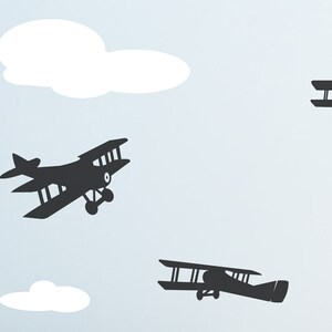 May include: Silhouettes of three black biplanes flying against a light blue background with white clouds.