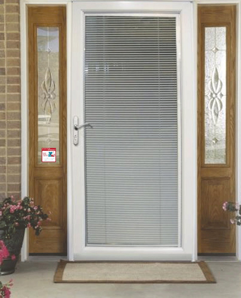 May include: White front door with a single pane of glass and a white door frame. The glass has white blinds inside. The door has a silver door handle and a small red and blue sticker on the door frame.