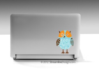 May include: A silver laptop computer with a blue and brown owl sticker on the lid. The owl has orange eyes and a white swirl pattern.