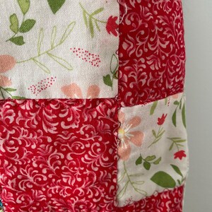 Pu&ograve; includere: Un tessuto patchwork caratterizzato da una griglia ripetitiva di quadrati di stoffa alternati. Un set di quadrati mostra uno sfondo bianco con un delicato motivo floreale nei toni del verde, rosa e rosso. L'altro set presenta uno sfondo rosso tinta unita con una stampa bianca di viticci e foglie vorticose.