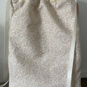Pu&ograve; includere: Una borsa rettangolare con coulisse in tessuto beige chiaro con un motivo ripetuto di foglie e viticci bianchi. La parte superiore &egrave; in tessuto color crema tinta unita con un'apertura arricciata, chiusa da due lunghi nastri di raso bianco.
