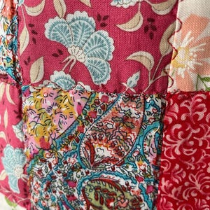 Pu&ograve; includere: Un tessuto patchwork caratterizzato da una variet&agrave; di motivi floreali e paisley in vivaci tonalit&agrave; di magenta, turchese, rosso e crema. I quadrati di tessuto sono uniti da cuciture visibili, creando una superficie strutturata e multicolore.