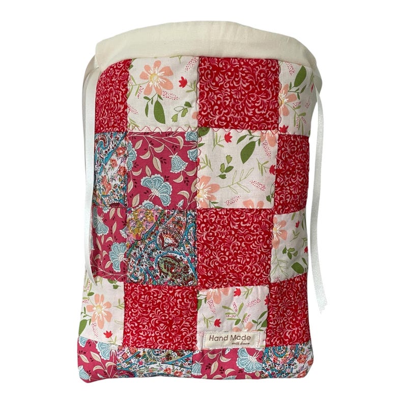 Pu&ograve; includere: Una borsa con coulisse caratterizzata da un design patchwork con vari motivi floreali e paisley nelle tonalit&agrave; del rosso, rosa, bianco e verde. La borsa presenta una parte superiore color crema con nastri bianchi e un'etichetta Hand Made with love.