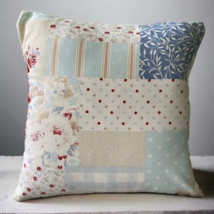 May include: A patchwork cushion with a variety of patterns in shades of blue, beige, and red. The cushion features floral, polka dot, striped, and plaid patterns.