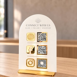 Puede incluir: Un letrero blanco arqueado con base dorada que presenta el texto CONNECT WITH US, SCAN, FOLLOW, DISCOVER y un icono de sol. Muestra tres iconos de redes sociales con bordes dorados y tres códigos QR en una cuadrícula vertical.