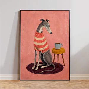 May include: A framed wall art print featuring a greyhound dog wearing a red and white striped jumper. The dog sits on a dark circular rug next to a small yellow stool holding a light blue mug. The background is a solid, textured dusty pink colour.