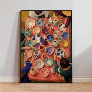 May include: A framed art print depicting a top-down view of a table covered with a pink cloth, featuring numerous colorful ceramic bowls, vases, and pitchers. Several pairs of hands are visible, interacting with the various pottery pieces.