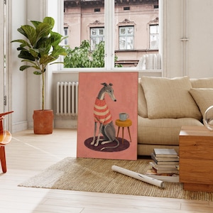 Puede incluir: Una impresi&oacute;n de arte mural rectangular que muestra a un galgo con un su&eacute;ter de rayas rojas y blancas, sentado sobre una alfombra circular oscura junto a un peque&ntilde;o taburete amarillo con una taza gris, sobre un fondo rosa s&oacute;lido y apagado.