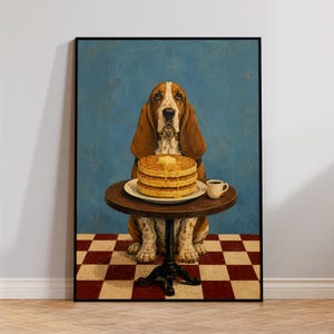 Puede incluir: Una impresión de arte mural enmarcada que muestra a un Basset Hound sentado en una mesa redonda pequeña. El perro está detrás de una pila de tres tortitas con un trozo de mantequilla y sirope, junto a una pequeña taza blanca de café negro.