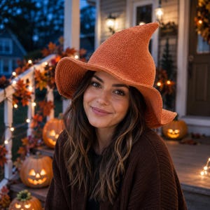 May include: A burnt orange knit hat with a tall, pointed crown and a wide, slightly curved brim. The hat features a textured, woven fabric construction with a distinct conical shape that tapers to a point at the top, providing a structured look.