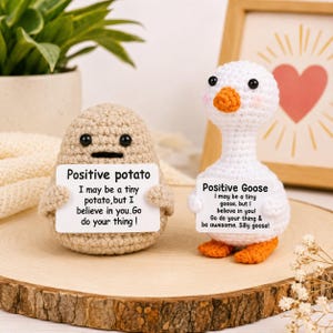 May include: A beige crocheted potato and a white crocheted goose, each holding a white sign. The potato sign reads: Positive potato, I may be a tiny potato, but I believe in you. Go do your thing! The goose sign reads: Positive Goose, I may be a tiny goose, but I believe in you! Go do your thing & be awesome. Silly goose!