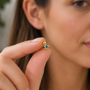 Peut inclure: Une boucle d'oreille à tige dorée en forme d'étoile à cinq branches avec un insert central bleu vif. La boucle d'oreille est dotée d'un petit fermoir sphérique et d'une tige fine, conçue pour le perçage, avec une finition métallique polie.