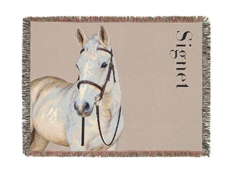 May include: A woven throw blanket featuring a light-colored horse wearing a dark brown bridle. The background is a solid tan color with the word Signet printed vertically in black on the right side. The blanket has a fringed edge.