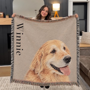 A woven throw blanket featuring a large, detailed portrait of a golden retriever dog with its tongue out. The name "Winnie" is printed vertically in black text on the left side. The blanket has a fringed edge with multicolored threads.