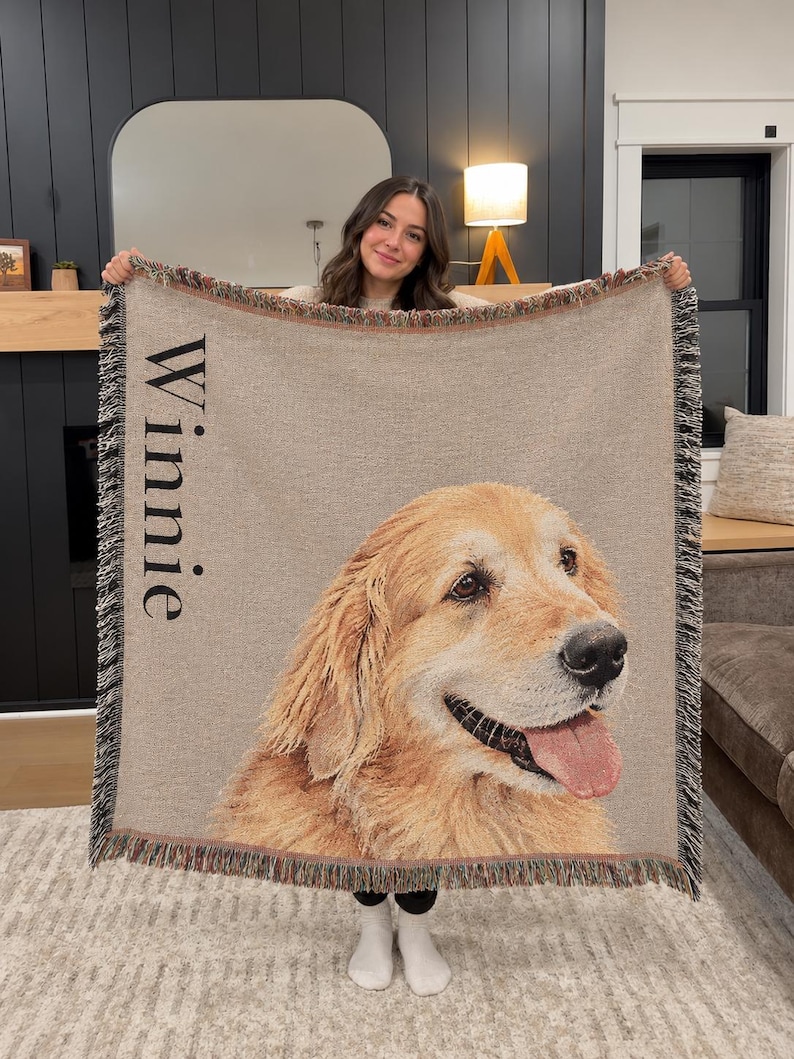 A woven throw blanket featuring a large, detailed portrait of a golden retriever dog with its tongue out. The name "Winnie" is printed vertically in black text on the left side. The blanket has a fringed edge with multicolored threads.