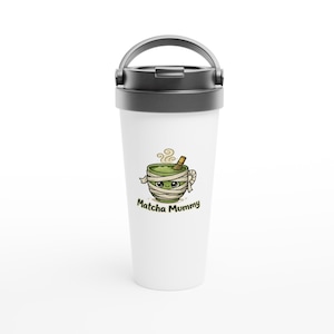 May include: A white travel tumbler with a black lid and handle featuring a graphic of a green matcha bowl wrapped in bandages like a mummy with a small whisk and the text Matcha Mummy printed in dark green letters below the illustration.
