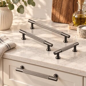 May include: Four matte black cabinet pulls with a cylindrical design and a textured, ribbed center section. Each handle features smooth, rounded ends and two sturdy mounting posts, providing a consistent look for kitchen or furniture hardware.